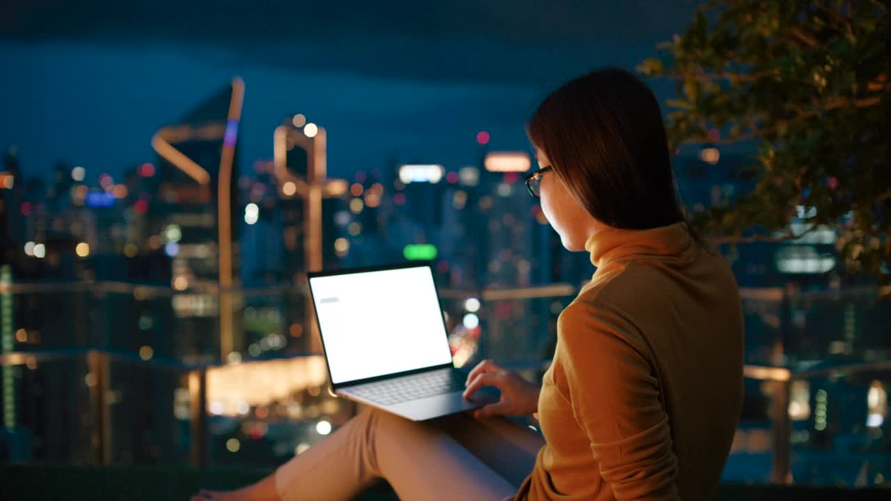 女人晚上坐在屋顶露台上，使用笔记本电脑视频素材