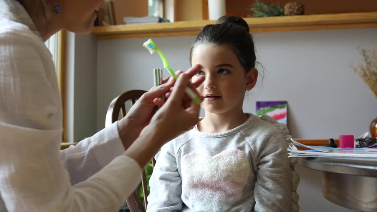 母亲用小刷子抚平5岁女儿的眉毛。视频素材
