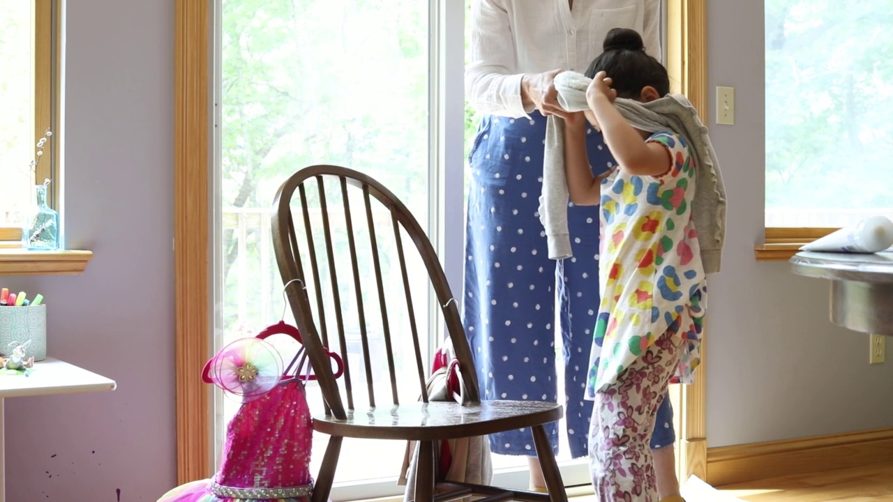 妈妈小心翼翼地给5岁的女儿脱去毛衣，女儿高兴地跳起舞来，准备穿上她的舞蹈服视频素材