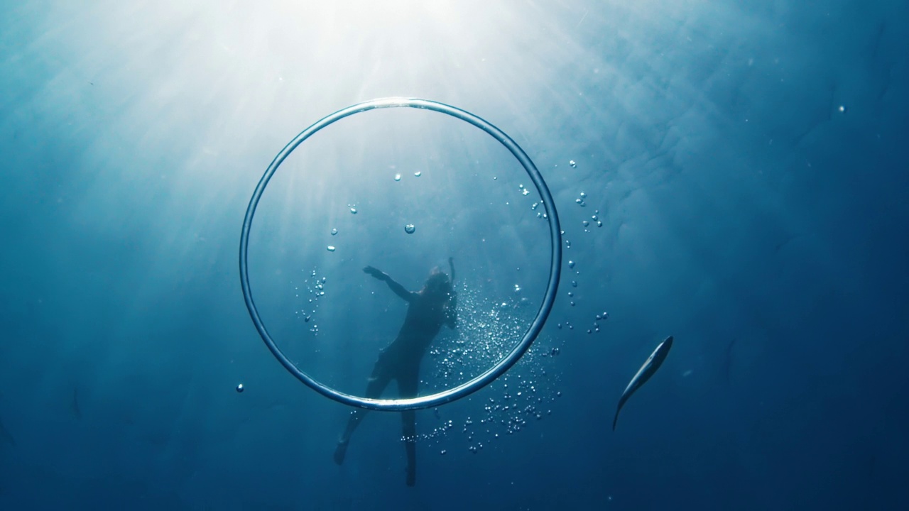 女人在海里游泳，看着鱼在环泡附近游动，在水下游向水面视频下载