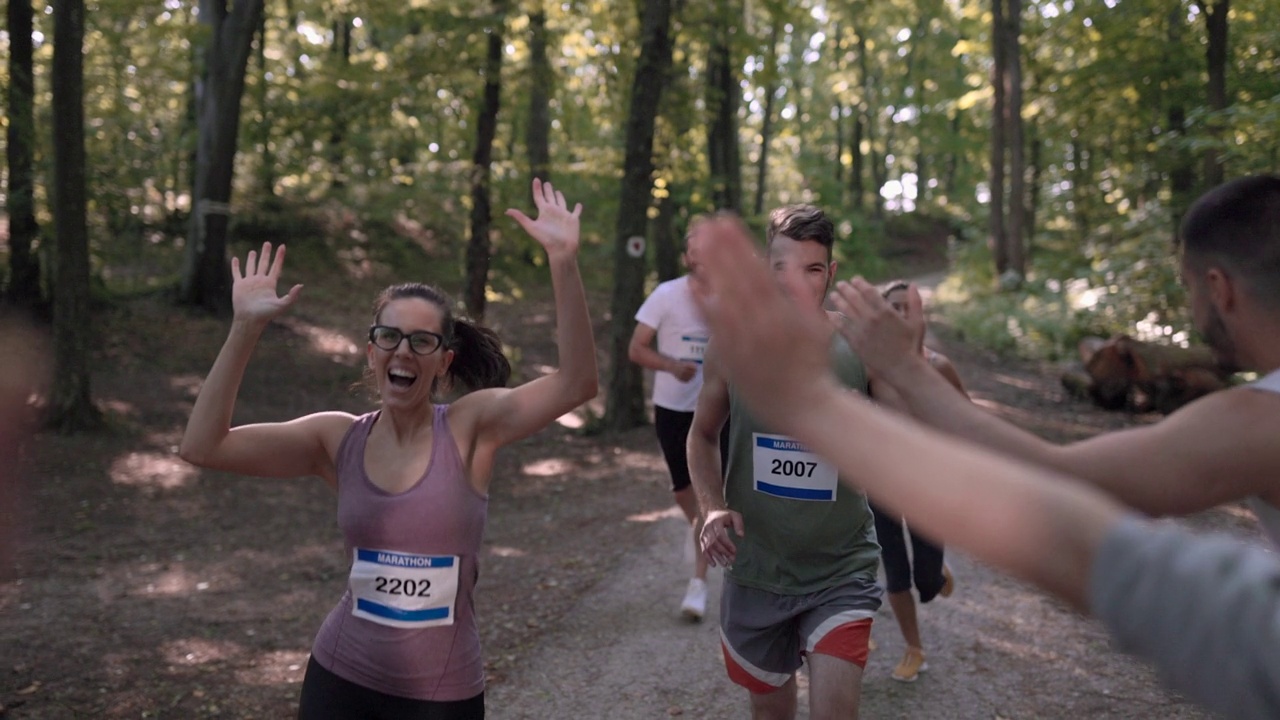 在马拉松比赛的终点线，快乐的女人问候一群运动员视频下载