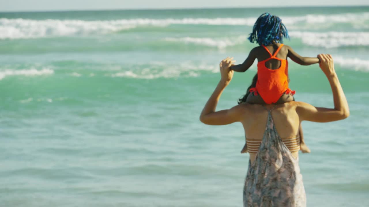 母亲肩上扛着女儿，在阳光明媚的夏日海洋视频素材