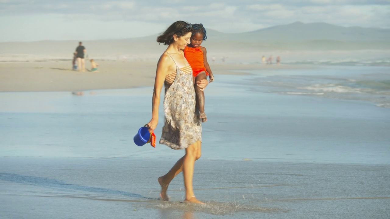 母亲和女儿走在阳光明媚的夏天的海洋冲浪视频素材