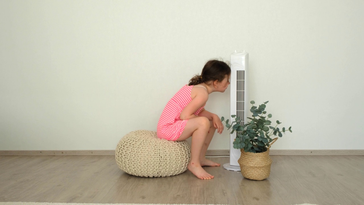 热，一个6岁的小女孩，坐在风扇旁边，躲避夏天的炎热。视频素材