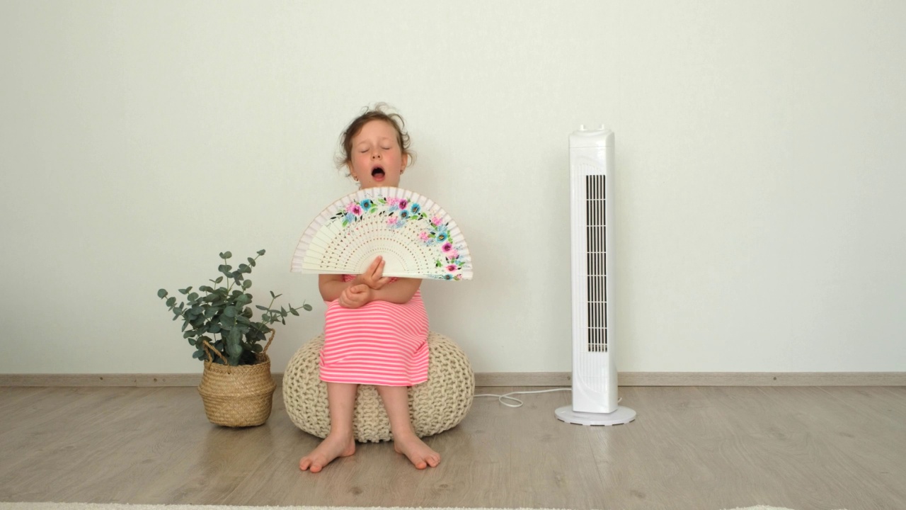 6岁的小女孩希特坐在电扇旁边，用电扇扇自己。躲避夏天的炎热。视频素材