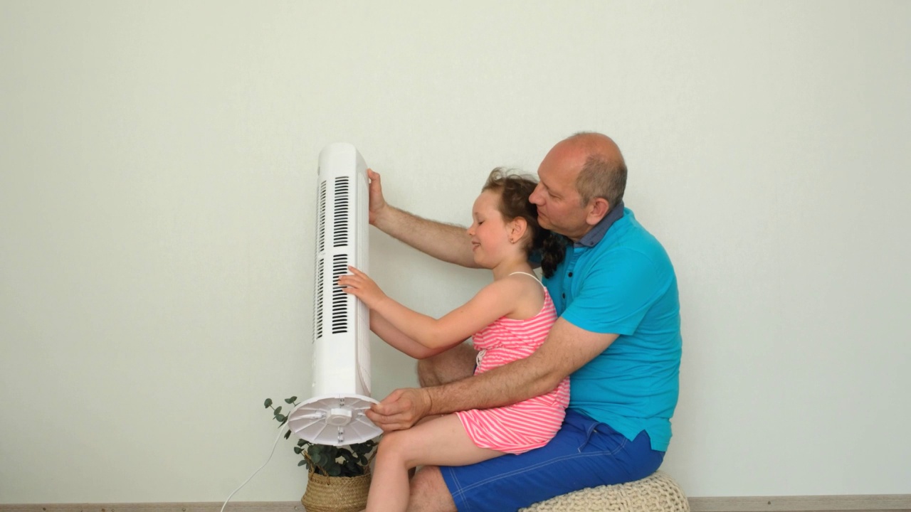 一个白人家庭，一个男人和一个孩子坐在风扇旁，躲避夏天的炎热。视频素材