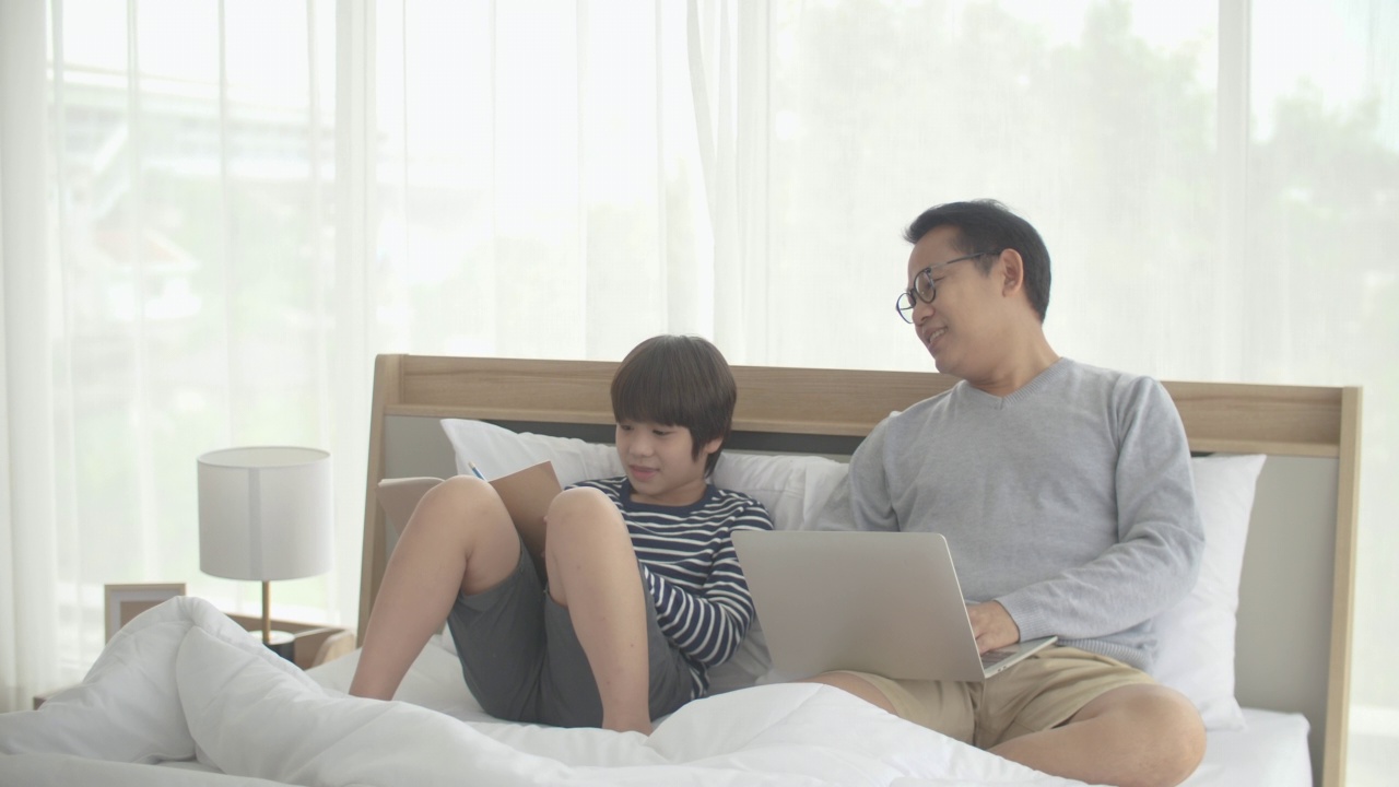 单亲父亲一边用笔记本电脑工作一边帮儿子做作业视频素材