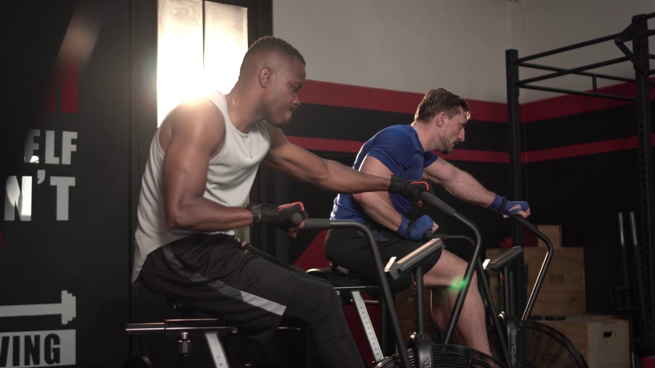 一个男人在健身房锻炼，两个男人在健身俱乐部骑室内自行车视频下载
