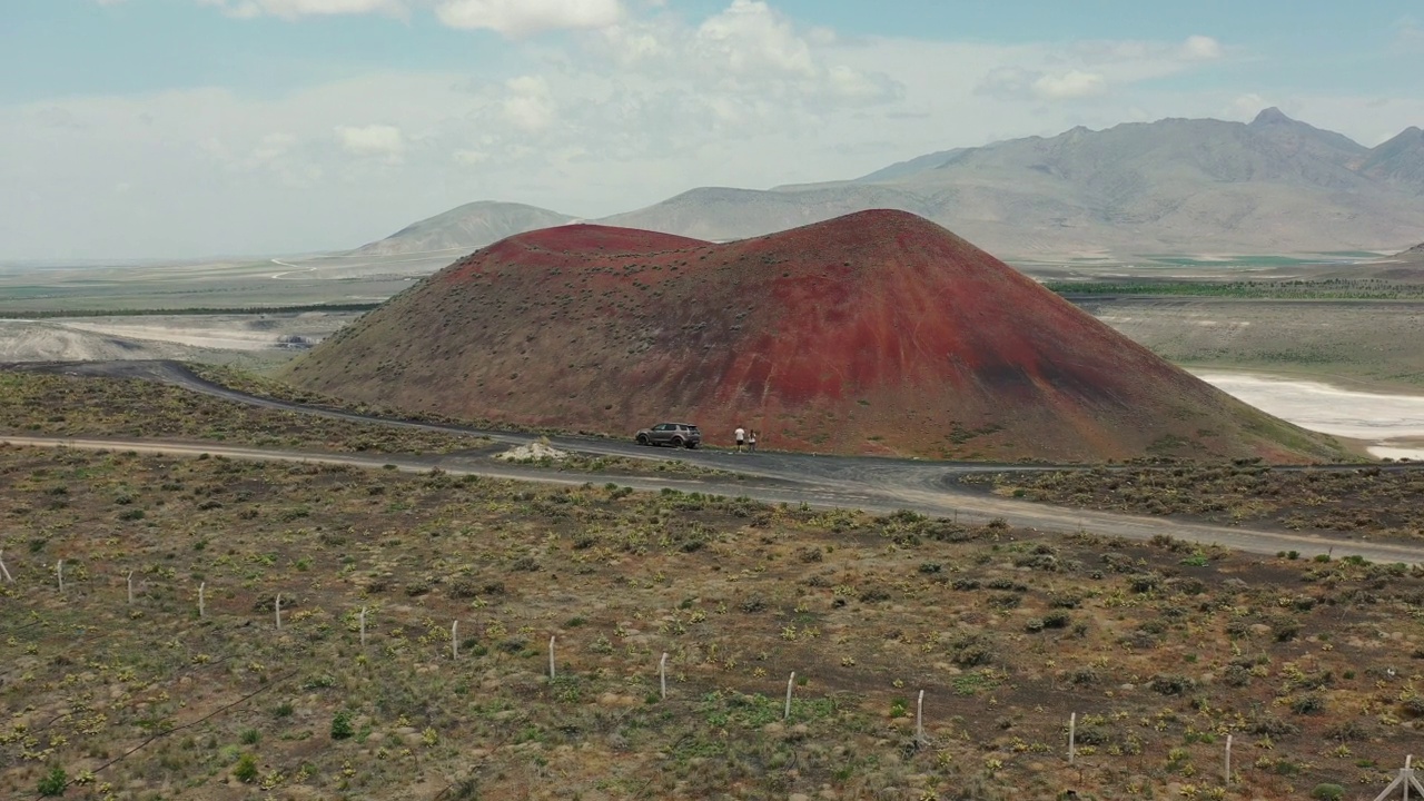 鸟瞰图，一名男子和一辆汽车在山顶上观看土耳其的红色火山口视频下载