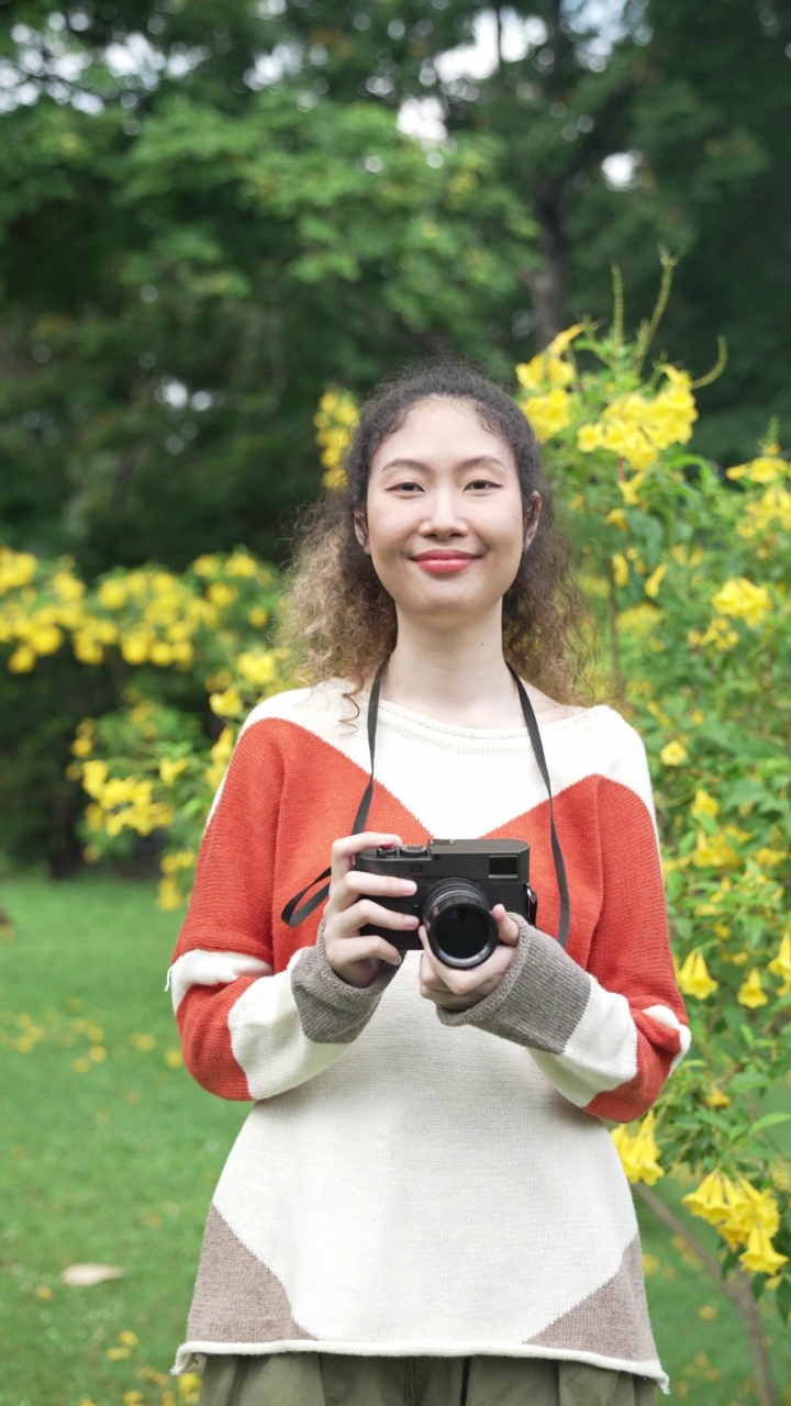 东南亚肖像垂直慢动作视频。亚洲女性独自旅行者使用相机在花园公园拍照。视频下载