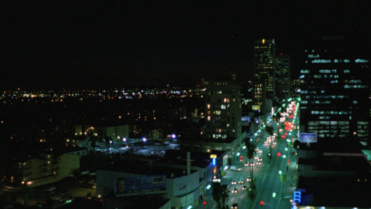 wilshire大道上的汽车大角度向下行驶。在洛杉矶。大灯，霓虹灯或标志和灯。BG的建筑。城市和城市街道。棕榈树排列在街道两旁视频素材