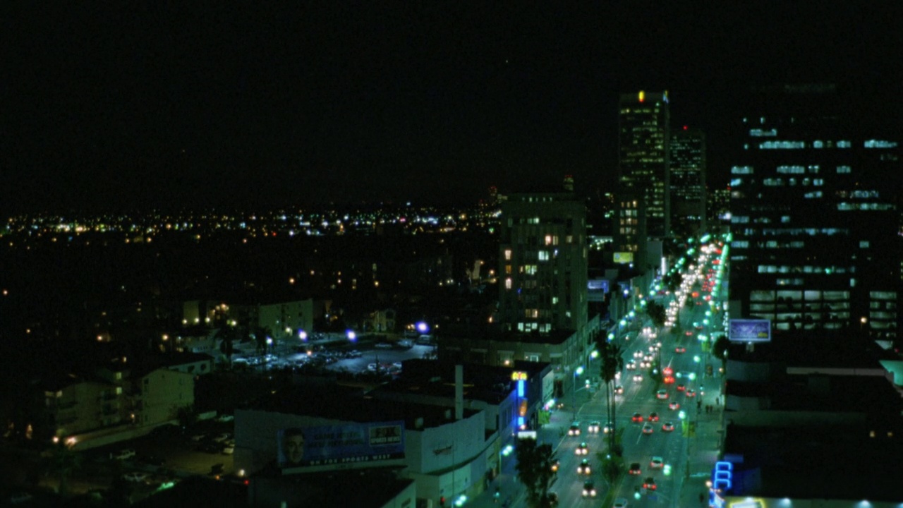wilshire大道上的汽车大角度向下行驶。在洛杉矶。车灯，霓虹灯或标志和城市灯光。BG的建筑。城市和城市街道。棕榈树排列在街道两旁视频素材