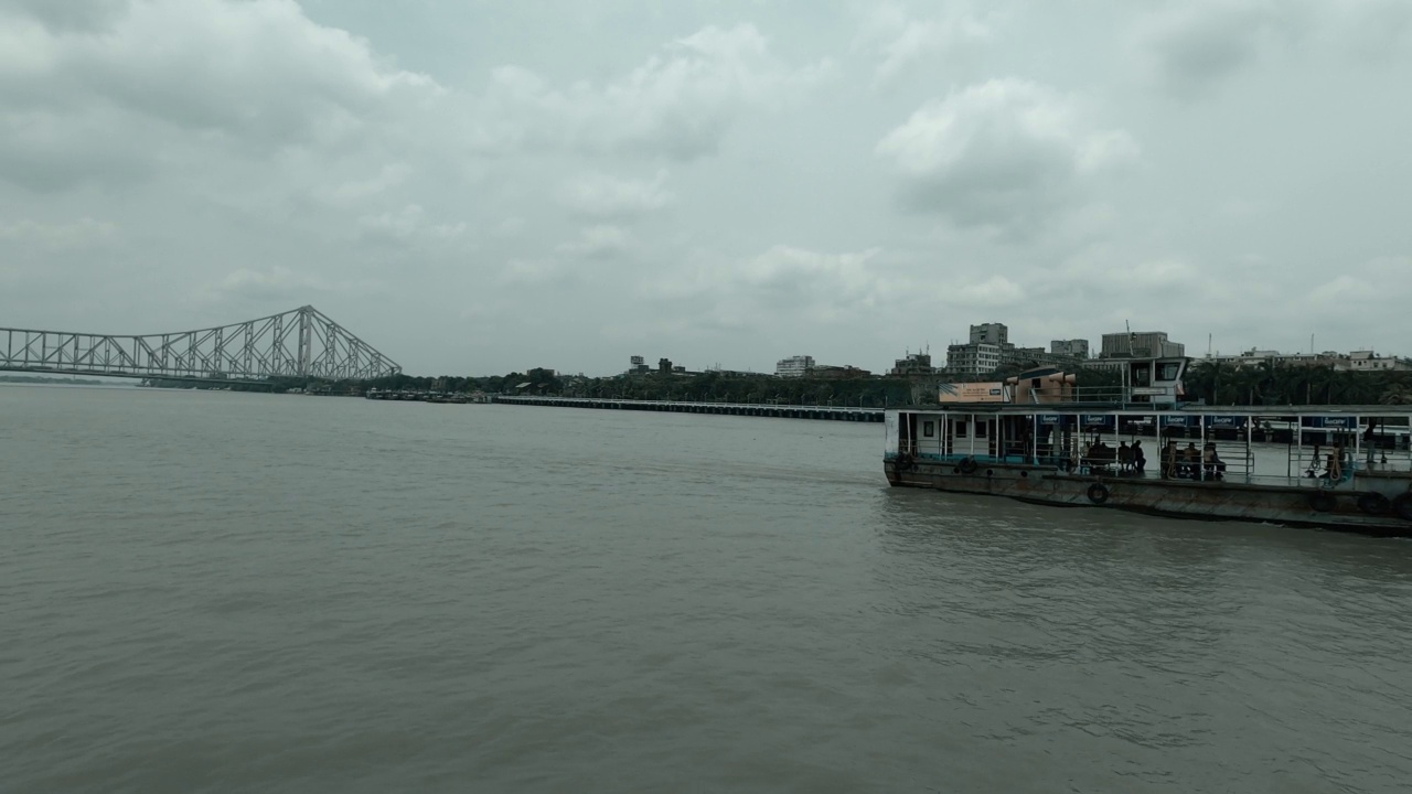 一艘渡船在胡格利河上航行，把豪拉桥抛在后面。从巴布大溪码头拍摄的画面。加尔各答西孟加拉印度南亚太平洋地区视频素材