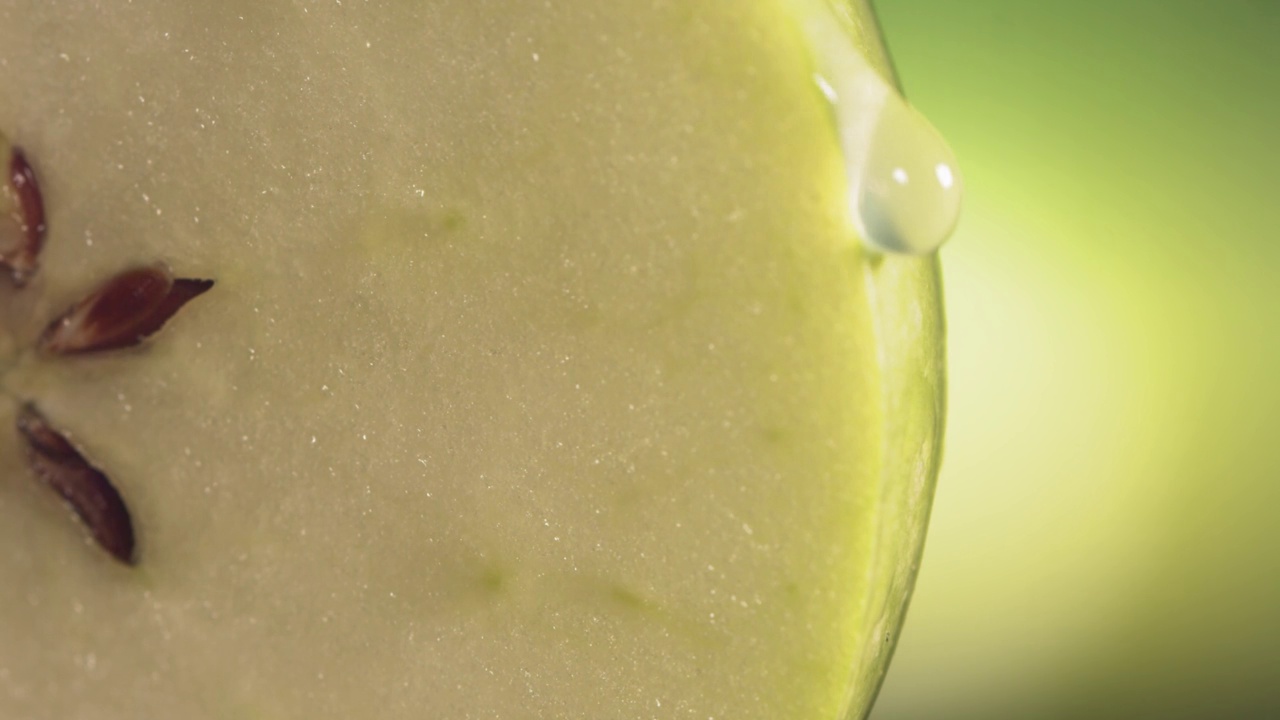 一滴水顺着成熟多汁的青苹果片的表面流下。慢镜头4 k视频下载