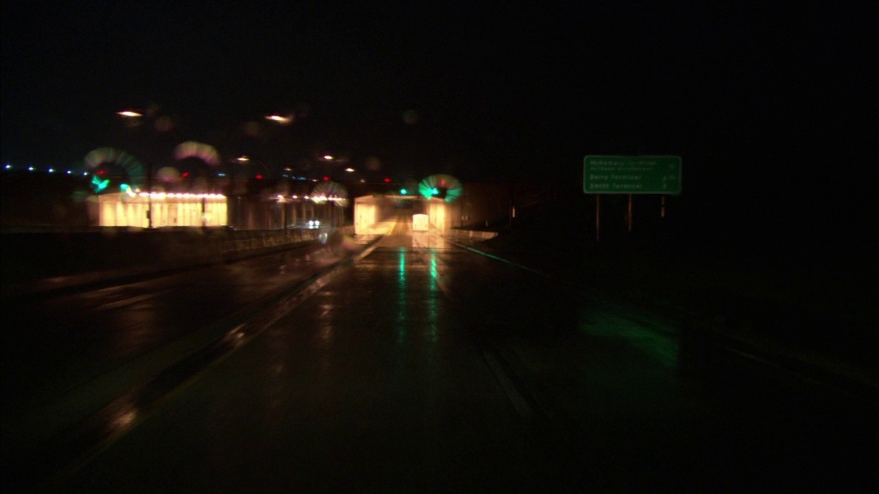 广角行驶在两车道潮湿的高速公路上。在“停车，租车前返回”的蓝色标志和红绿灯下通过。看到雨点落在挡风玻璃和雨刷上。看高速公路标志，灯柱和水泥视频素材