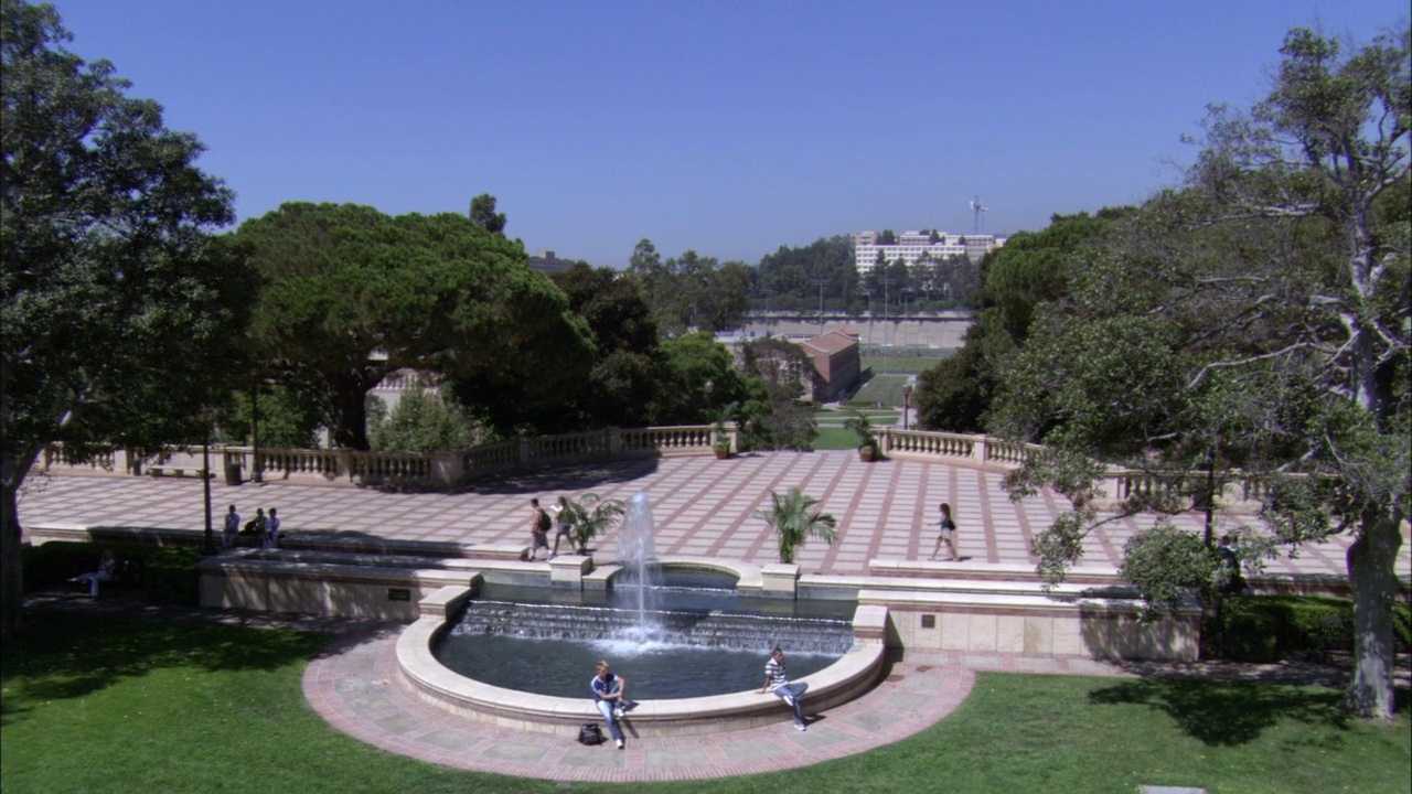 加州大学洛杉矶分校校园广场和喷泉的高角度。学生们步行的砖混广场周围环绕着树木。田径场和宿舍，宿舍在bg。喷泉在前景喷水。大学视频素材