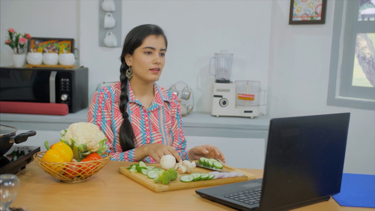 一个印度女孩在厨房里切菜，忙着回复信息视频素材
