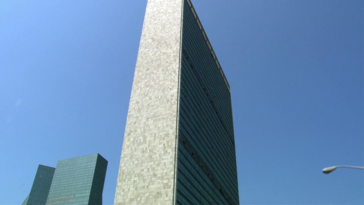 联合国总部、秘书处大楼上角。看到晴朗的蓝天在bg。看到路灯。在街上行驶的车里有摄像头。看见车左转。红砖建筑简介视频下载