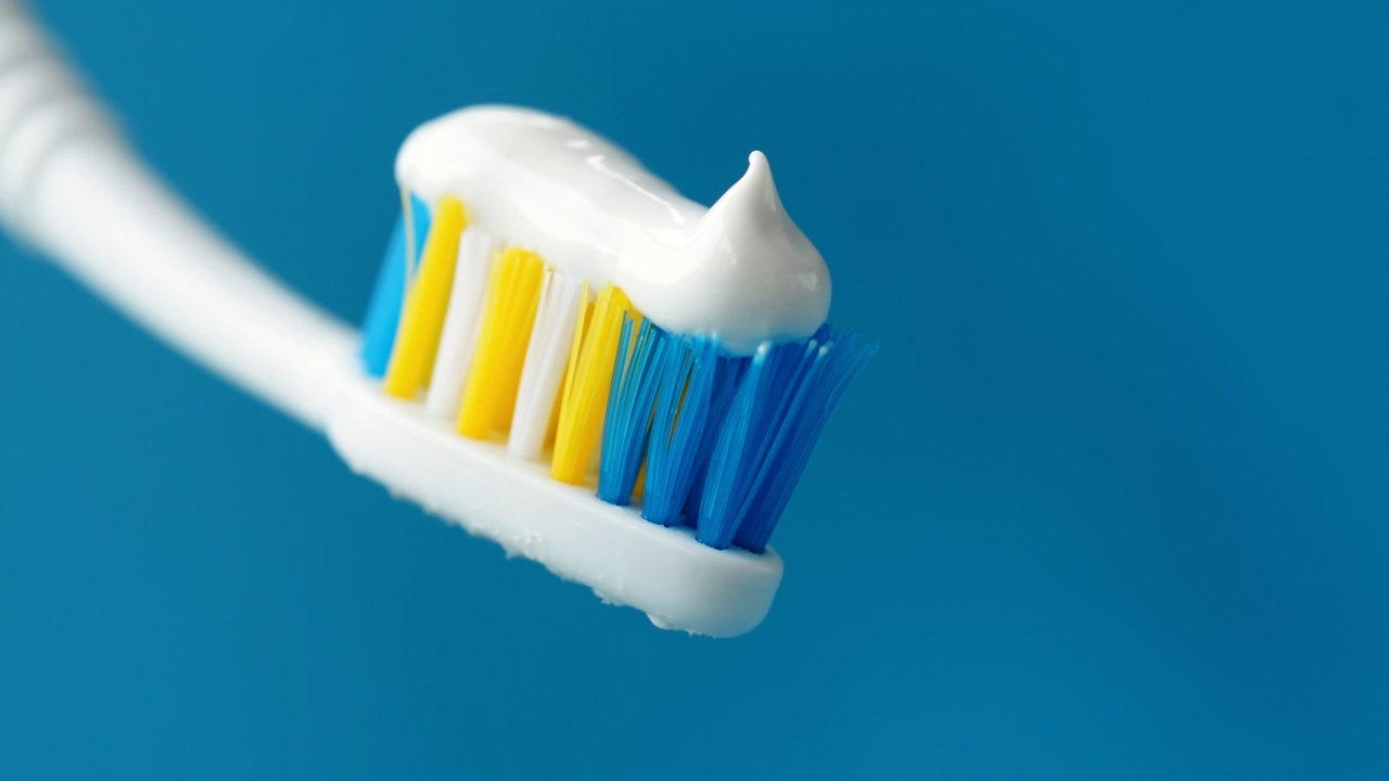 白色的牙膏在蓝色的背景上用牙刷从牙膏管中挤出来，牙膏末端有一个美丽的卷发。4k原始宏视频。视频下载