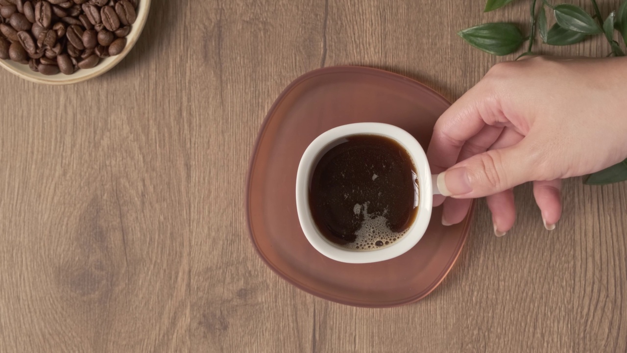 4k视频，平板咖啡白色杯在木制桌面。特浓咖啡热饮健康。在咖啡馆或家里的桌子上放一盆绿色植物。女手拿一杯热气腾腾的咖啡喝完而空杯视频素材