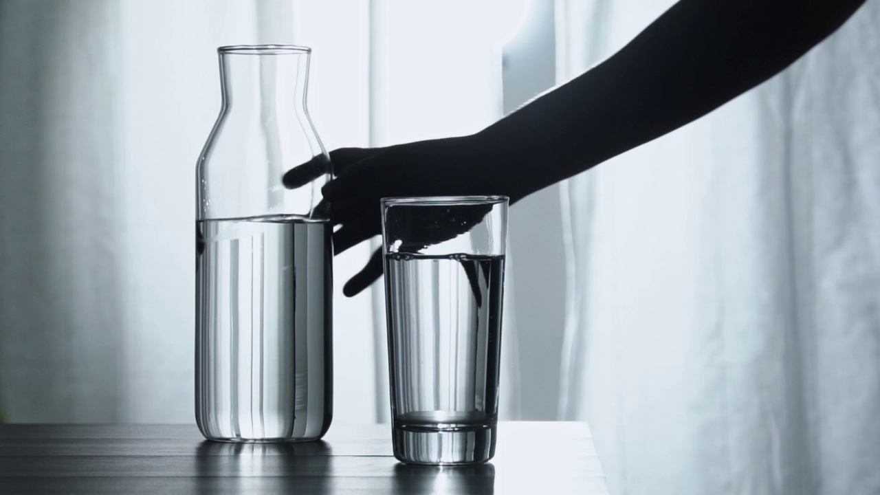 女人的手从瓶子里倒新鲜的纯净水到桌子上的杯子里，健康和饮食的概念，慢动作镜头视频素材
