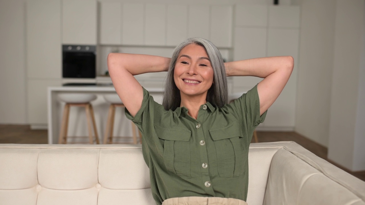 宁静悠闲的中年妇女与长灰色头发坐在沙发在现代公寓视频素材