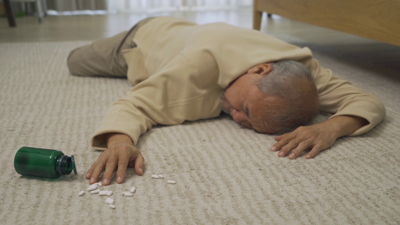 年老的老人生病的资深亚洲人摔倒在地板上，试图从事故在家里的卧室或房子里得到药。人。健康问题。视频下载