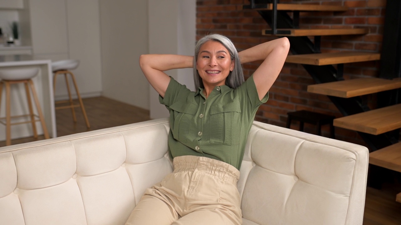 宁静悠闲的中年妇女与长灰色头发坐在沙发在现代公寓视频素材