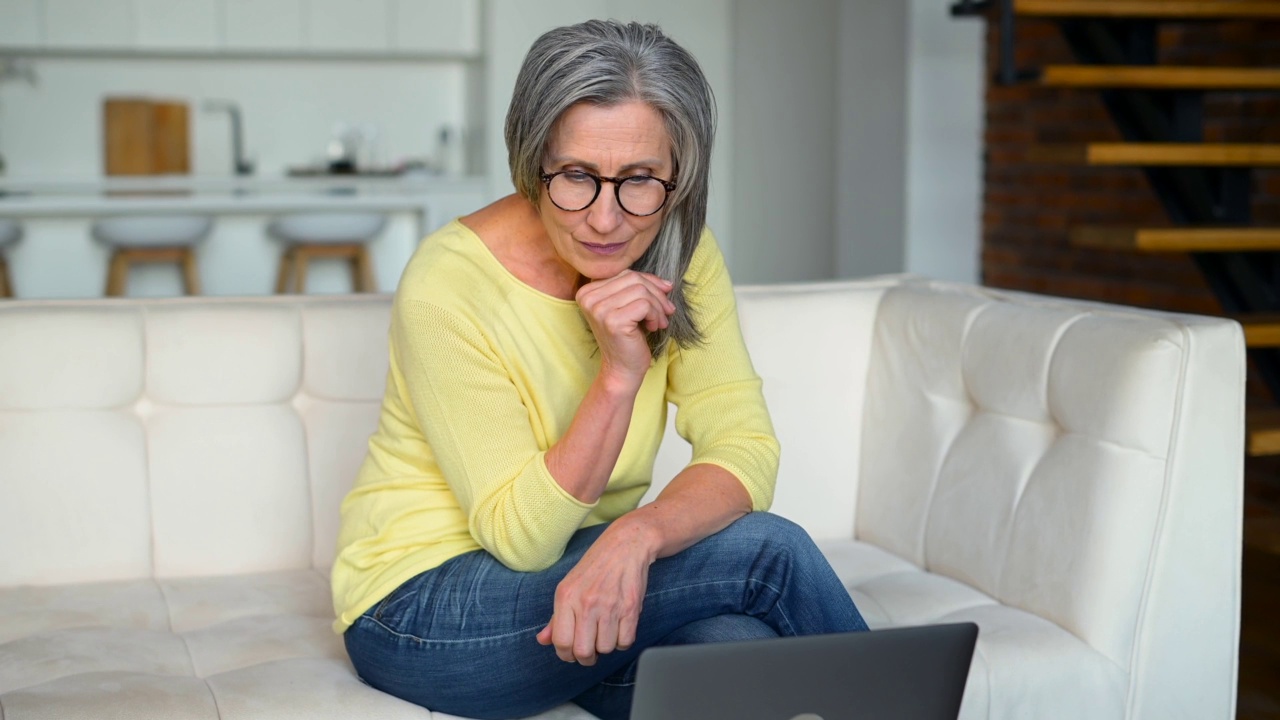 乐观的成熟中年女性在闲暇时间在家使用笔记本电脑视频素材
