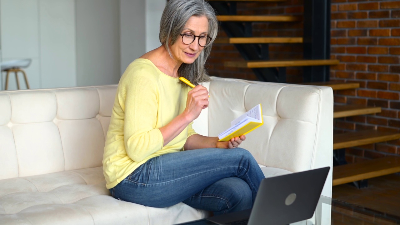 集中成熟的灰色头发的女人戴着眼镜使用笔记本电脑在线学习视频素材