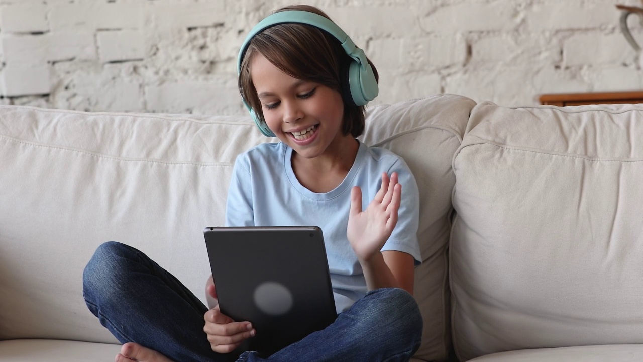 快乐的Z一代博主孩子戴着无线耳机用平板电脑视频素材