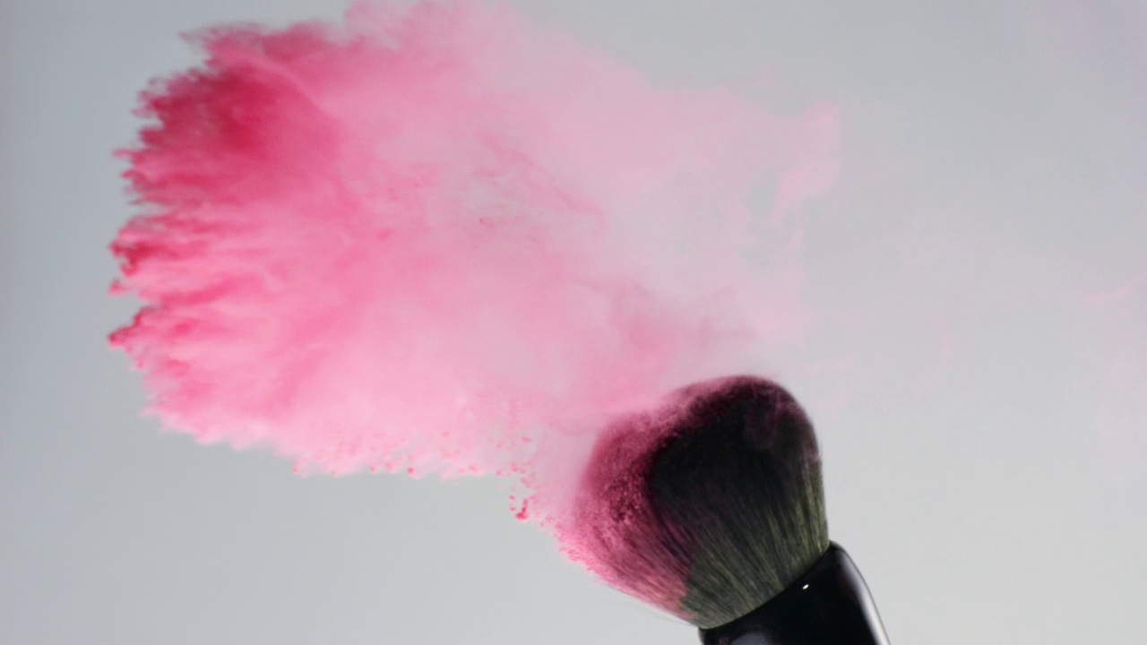特写和超慢的动作，粉红色的粉末爆炸和飞溅从摇摆的化妆刷在灰色的背景视频素材