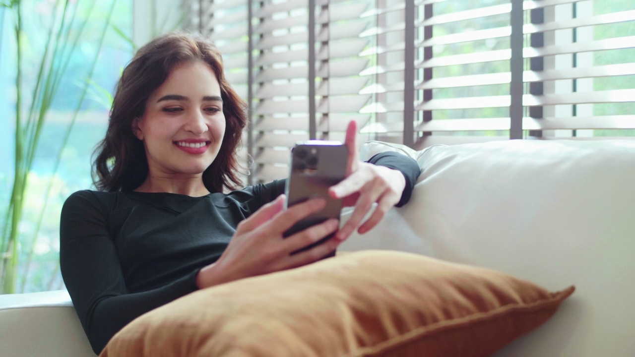 年轻快乐的女人用智能手机看着屏幕，笑着给朋友发短信视频素材