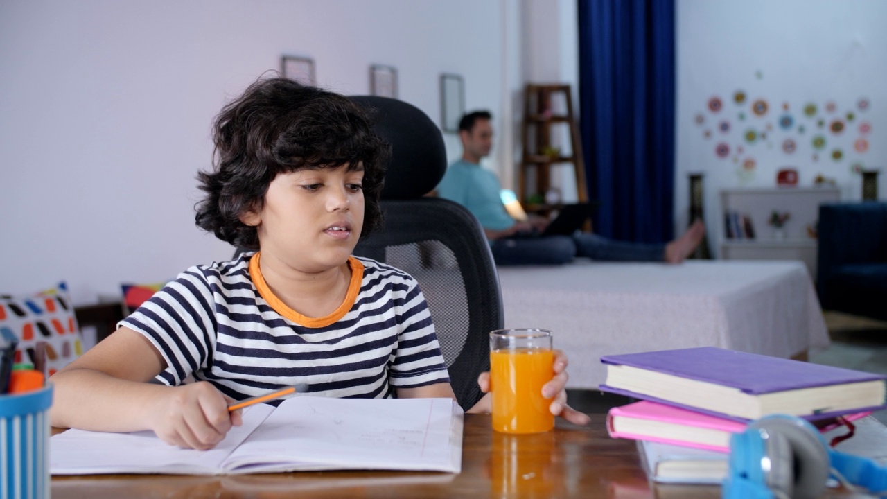 一头卷发的小男孩一边做作业，一边喝着果汁视频素材
