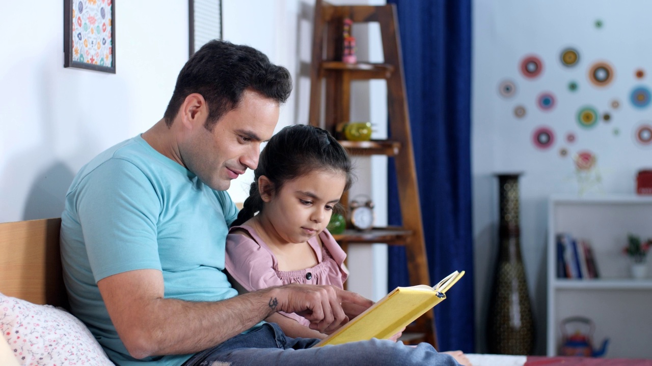 一位年轻的印度父亲和他的小女儿正在读一本书——晚上的故事、就寝时间、过去最喜欢的时间、孩子的教育视频素材