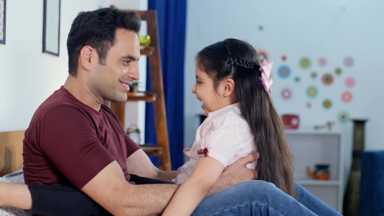 一个印度漂亮的小女孩坐在她父亲的腿上和他一起玩——在一起和建立联系，睡前玩耍视频素材