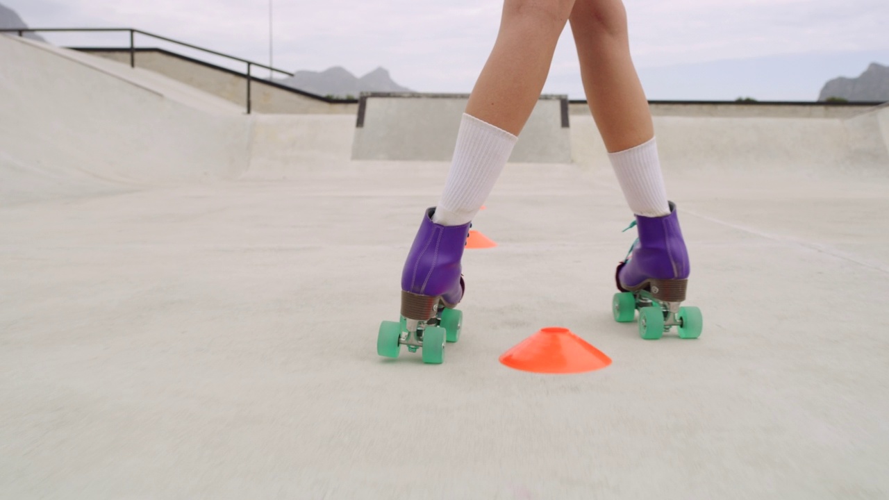 特写的女性腿轮滑在一个滑冰公园外面。熟练的滑冰女孩或人骑快速通过锥。穿着老式的彩色轮滑鞋练习体育比赛视频素材