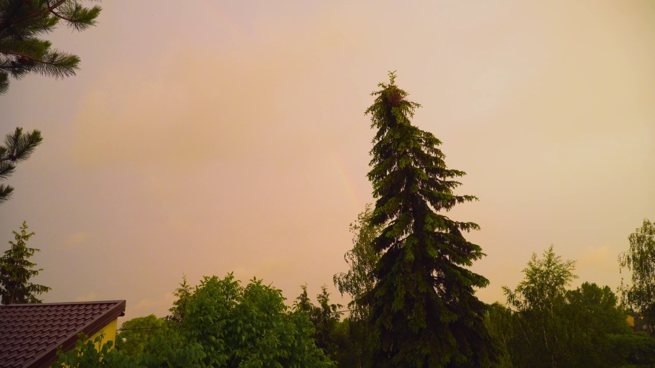 强烈风暴后的蓝色黄色云彩，背景是高高的松树和屋顶上的彩虹碎片视频素材
