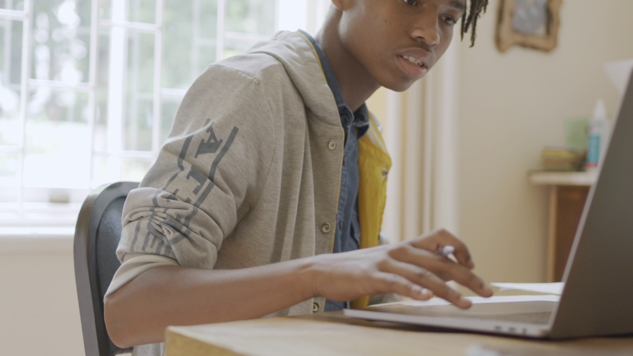 十几岁的男孩在家里的书桌上用笔记本电脑做作业视频素材