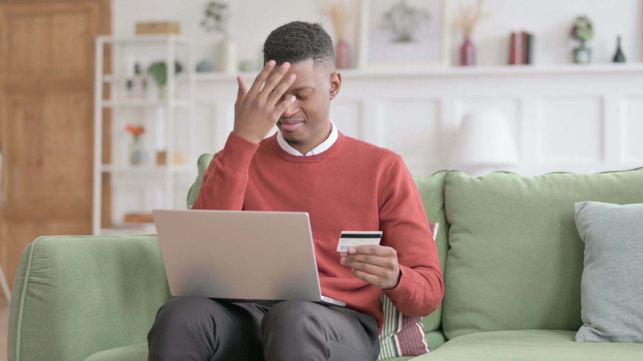 非洲男子在沙发上的笔记本电脑上在线支付失败视频素材