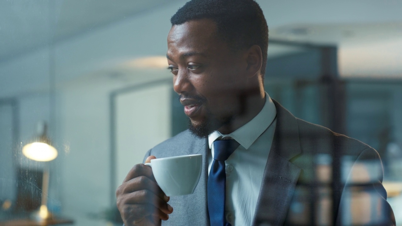 自信的商人，看上去若有所思，站在现代化的办公室里喝着咖啡。一位职业男性企业家和商界领袖，一边喝茶，一边享受休息视频素材