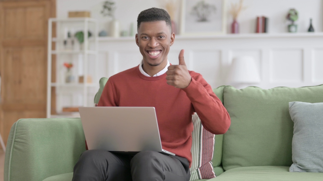 非洲男子在沙发上使用笔记本电脑时竖起大拇指视频素材