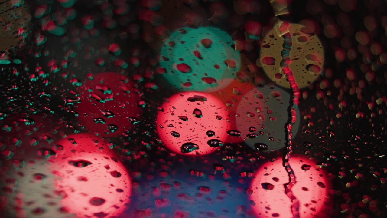 雨水打在汽车的挡风玻璃上，红色的散景在夜间变成绿色的散景。视频下载