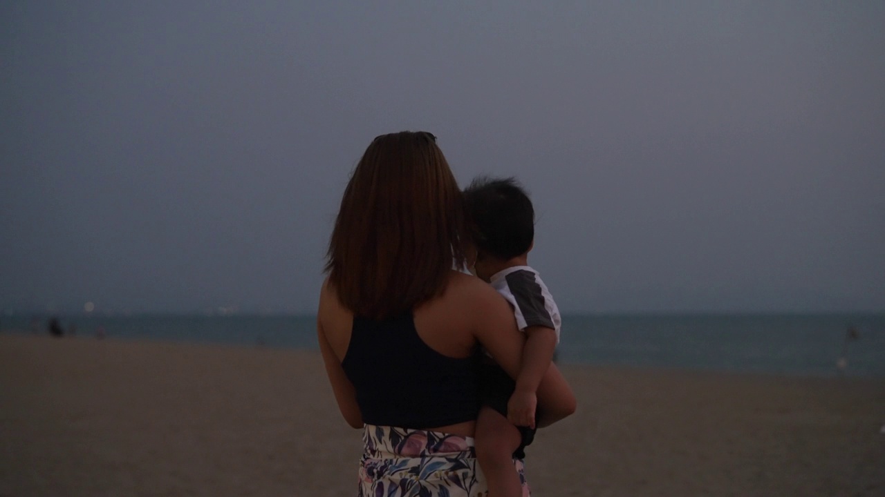 年轻的亚洲母亲带着她的孩子在晚上欣赏海滩景色。视频下载