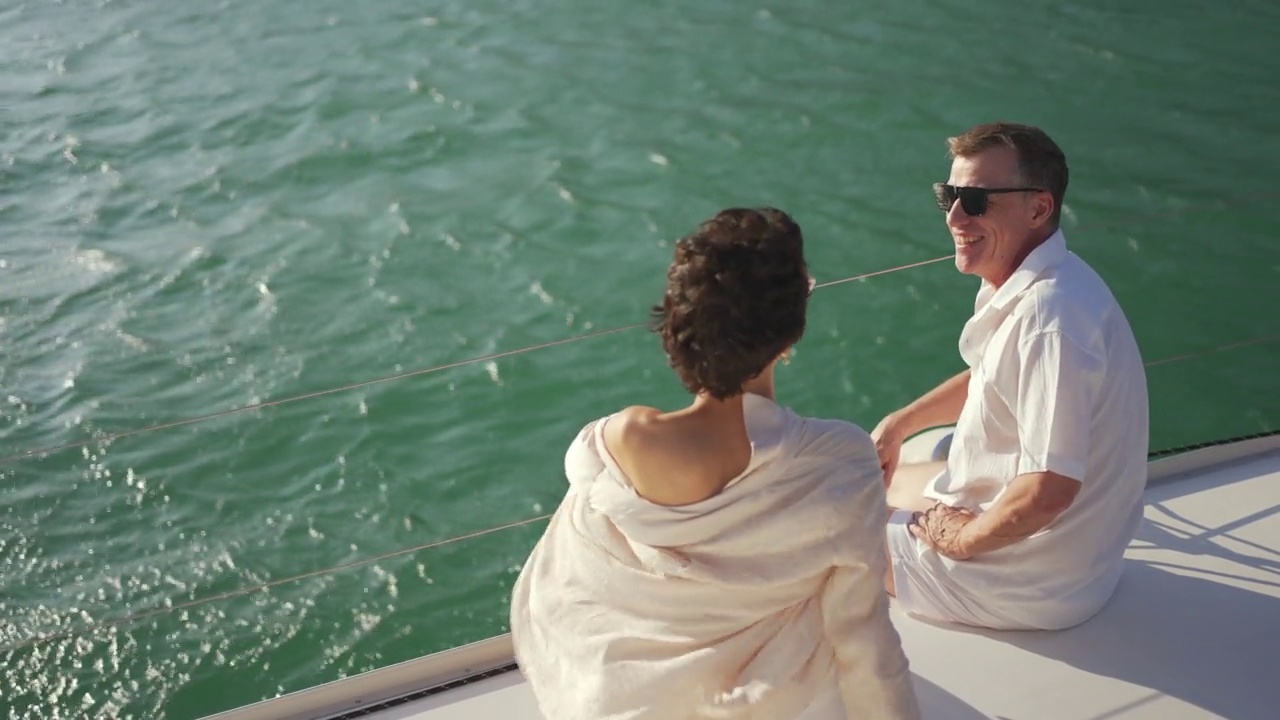 在夏天的夕阳下，一对白人夫妇喝着香槟，乘坐双体船在海上航行。视频素材