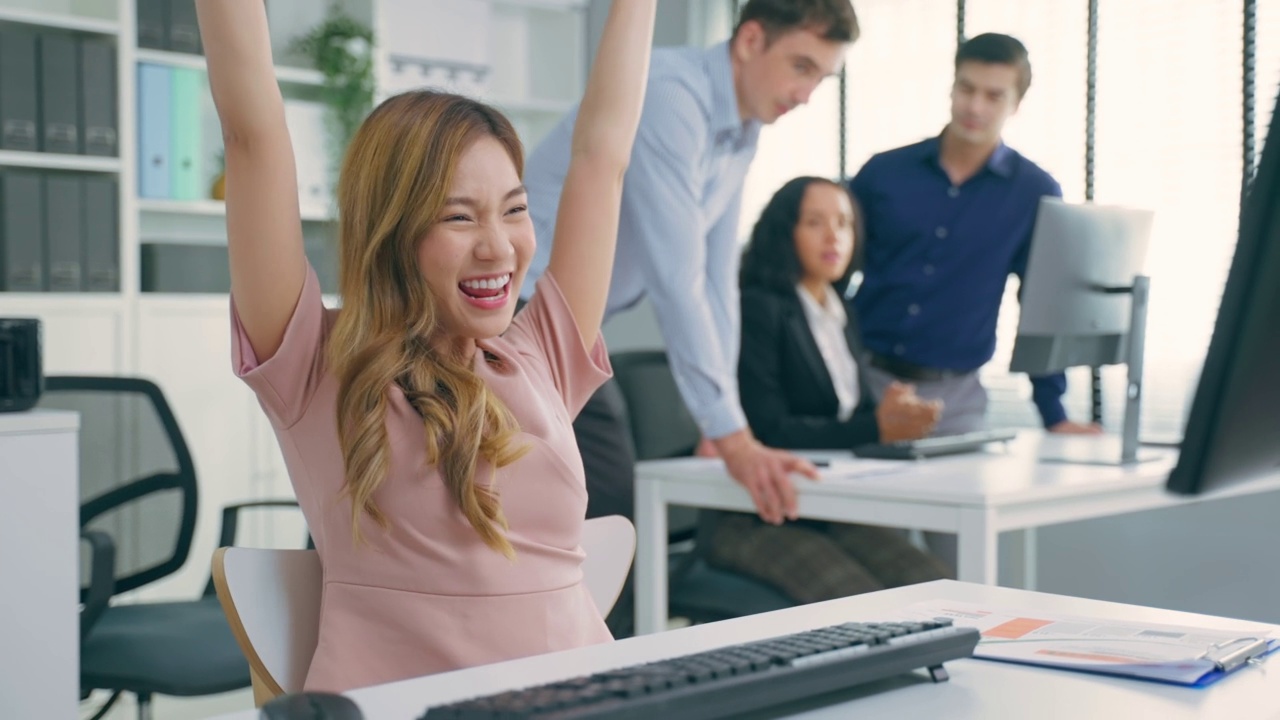 亚洲美丽的商业女性微笑感到快乐，而在办公室工作。有魅力的专业女员工穿着正装坐在工作场所的桌子上，使用笔记本电脑享受在公司。视频下载