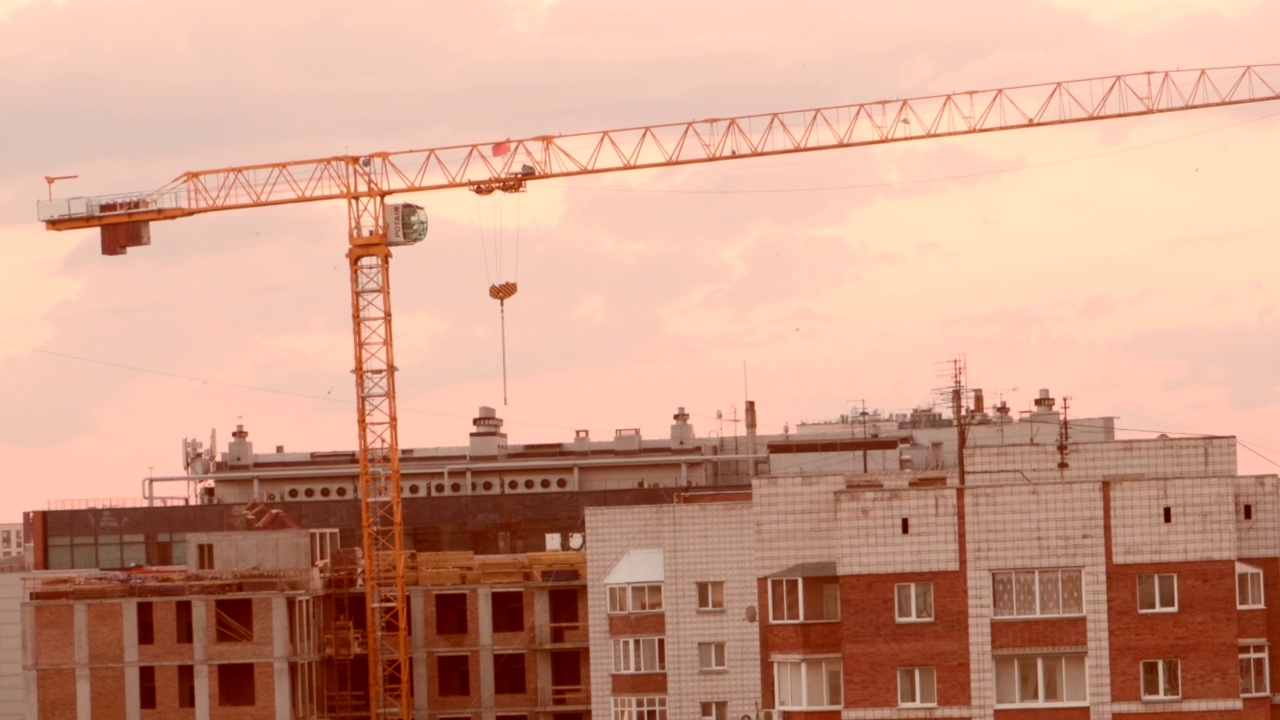 建筑工地上高大的起重机和房子，映衬着天空粉红色的夕阳视频素材