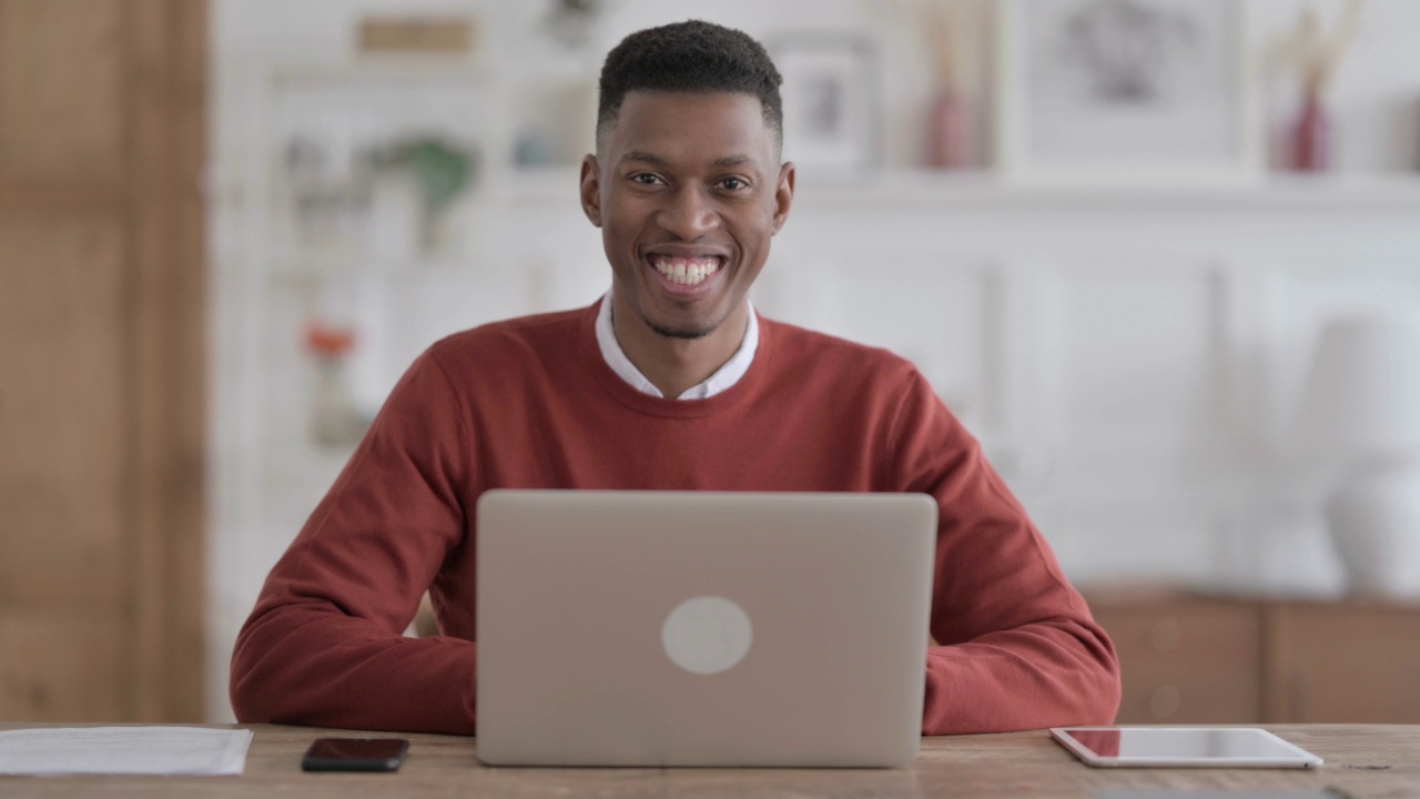 非洲男子在办公室使用笔记本电脑时对着相机微笑视频素材