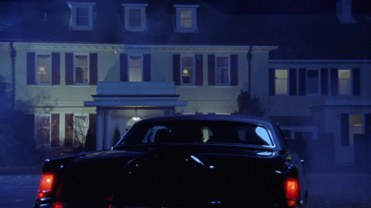 一辆黑色轿车在上层住宅的环形车道上不规则地转弯的广角。打开前灯。汽车启动和停止了几次，然后转身和停止。车里有几个人。三层的房子。雾或雾。秋天。NEGATIV视频下载