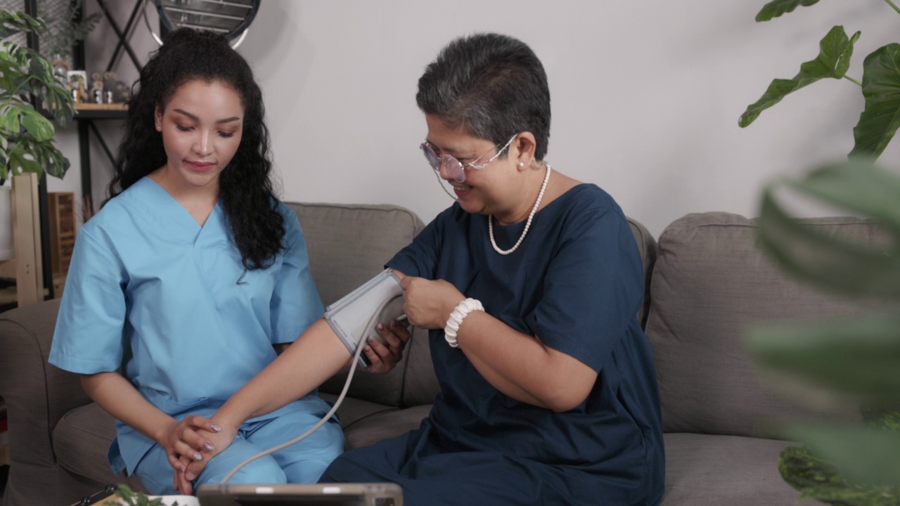 在家里的客厅里，护士在一位亚洲老人身上使用血压计。在家提供医疗服务。照顾老年病人。个人护理业务。养老院视频素材